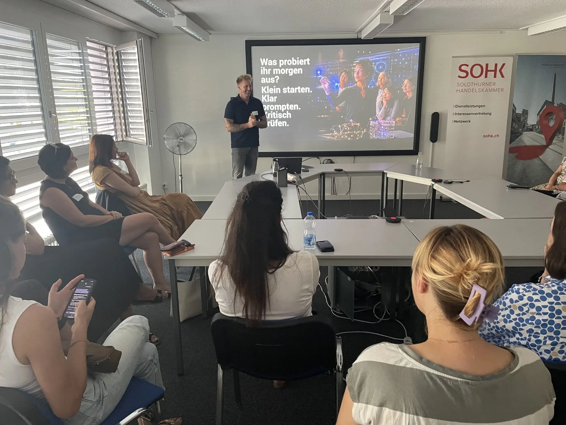 Dr. Benjamin Hermberg leitet einen KI-Workshop, auf der Leinwand: «Klein starten. Klar prompten. Kritisch prüfen.»